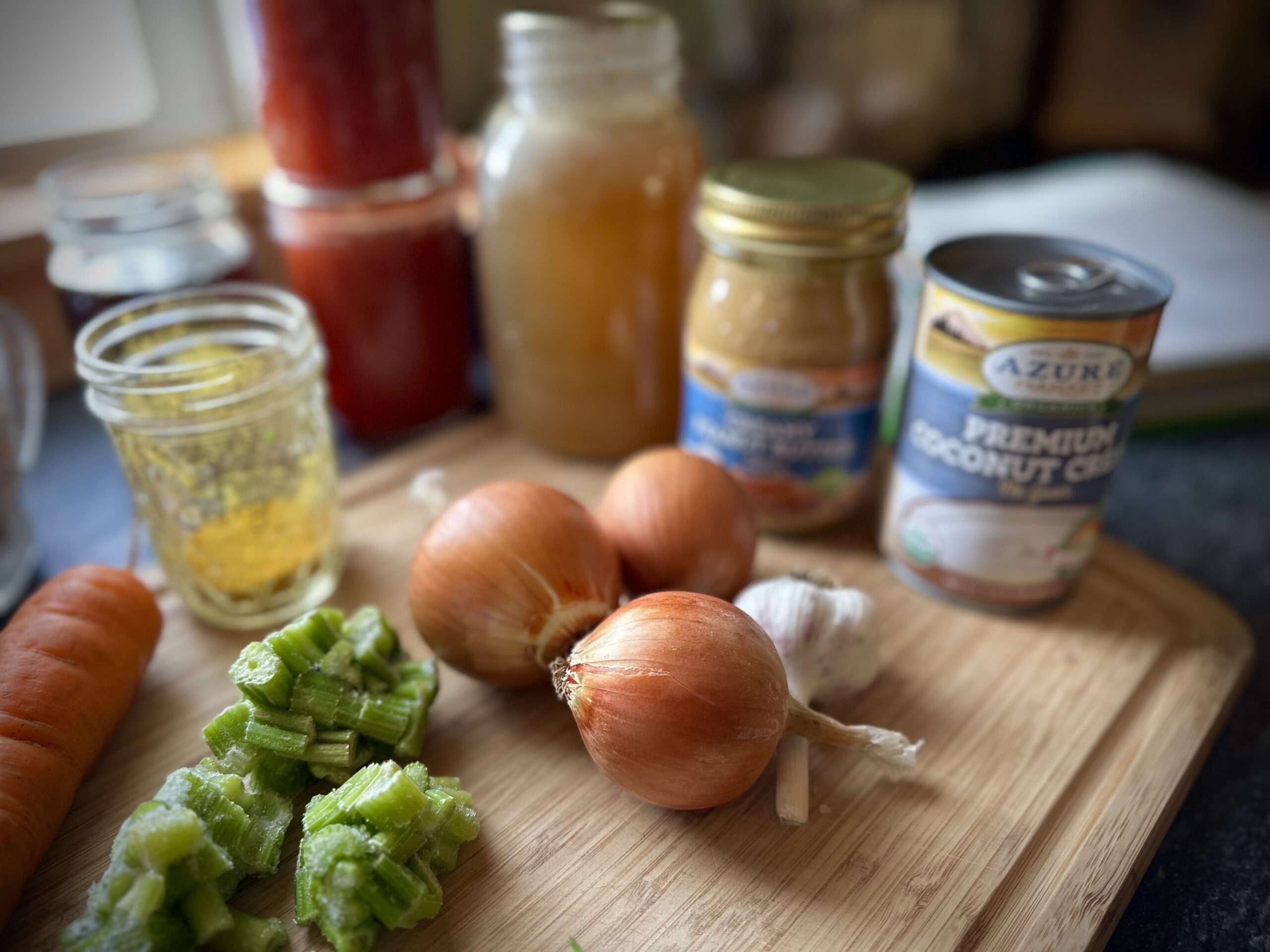 Ingredients for Senegalese peanut stew on a cutting board, including onions, garlic, celery, peanut butter, broth, and coconut milk.