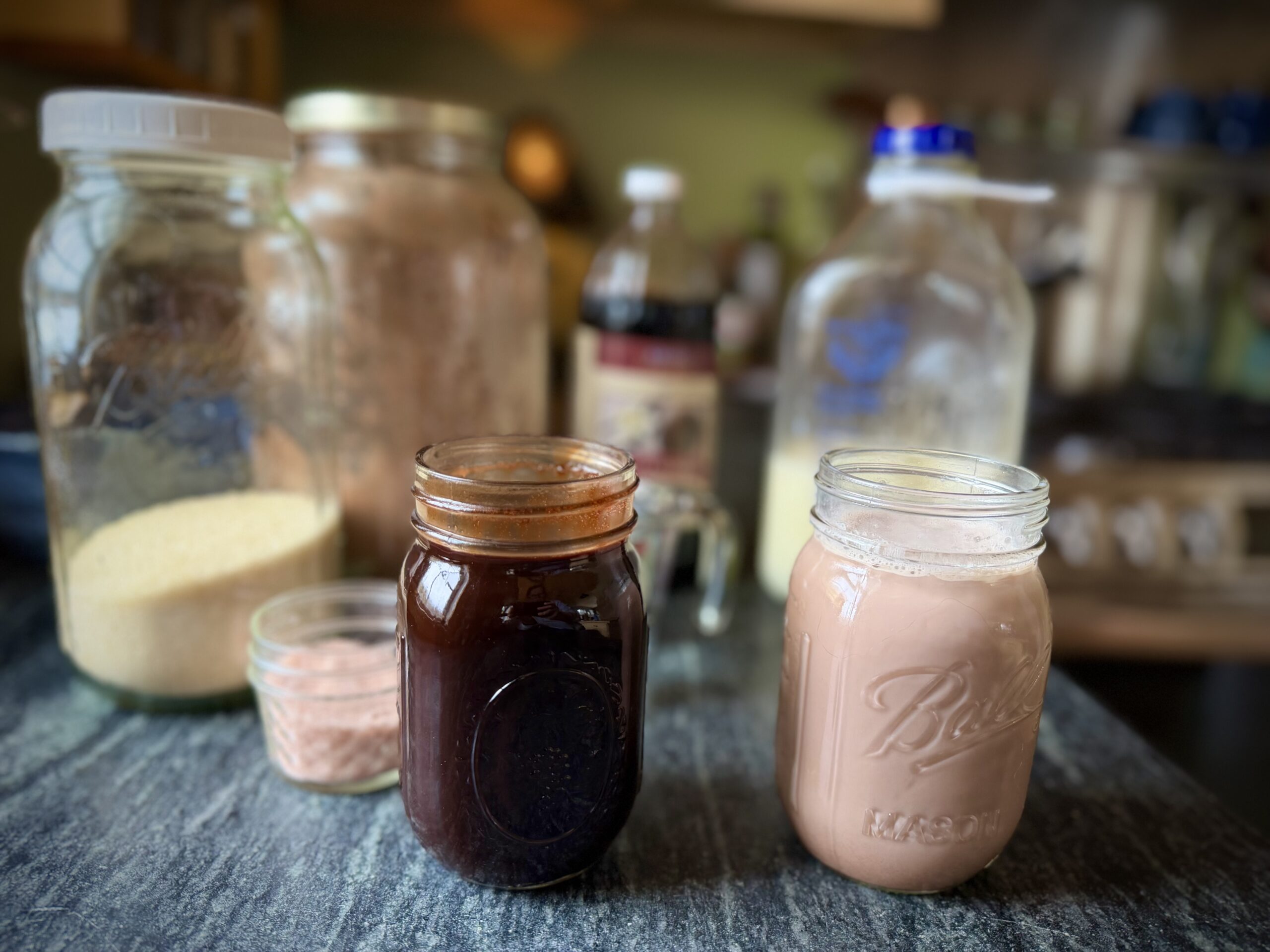 Homemade chocolate syrup in a mason jar next to a jar of chocolate milk made with raw milk