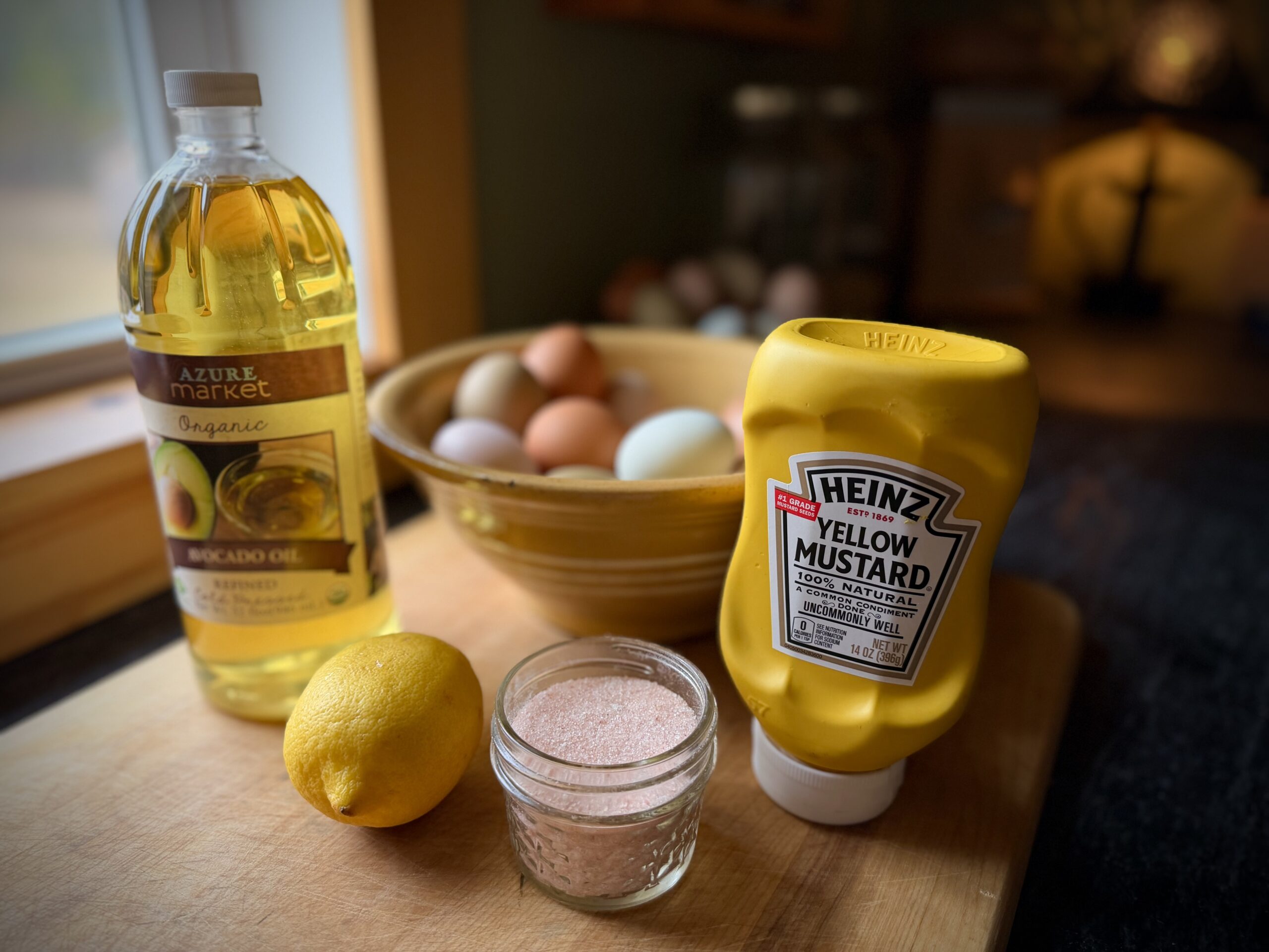 homemade mayonnaise ingredients with avocado oil, egg, lemon, mustard, and salt on wooden board