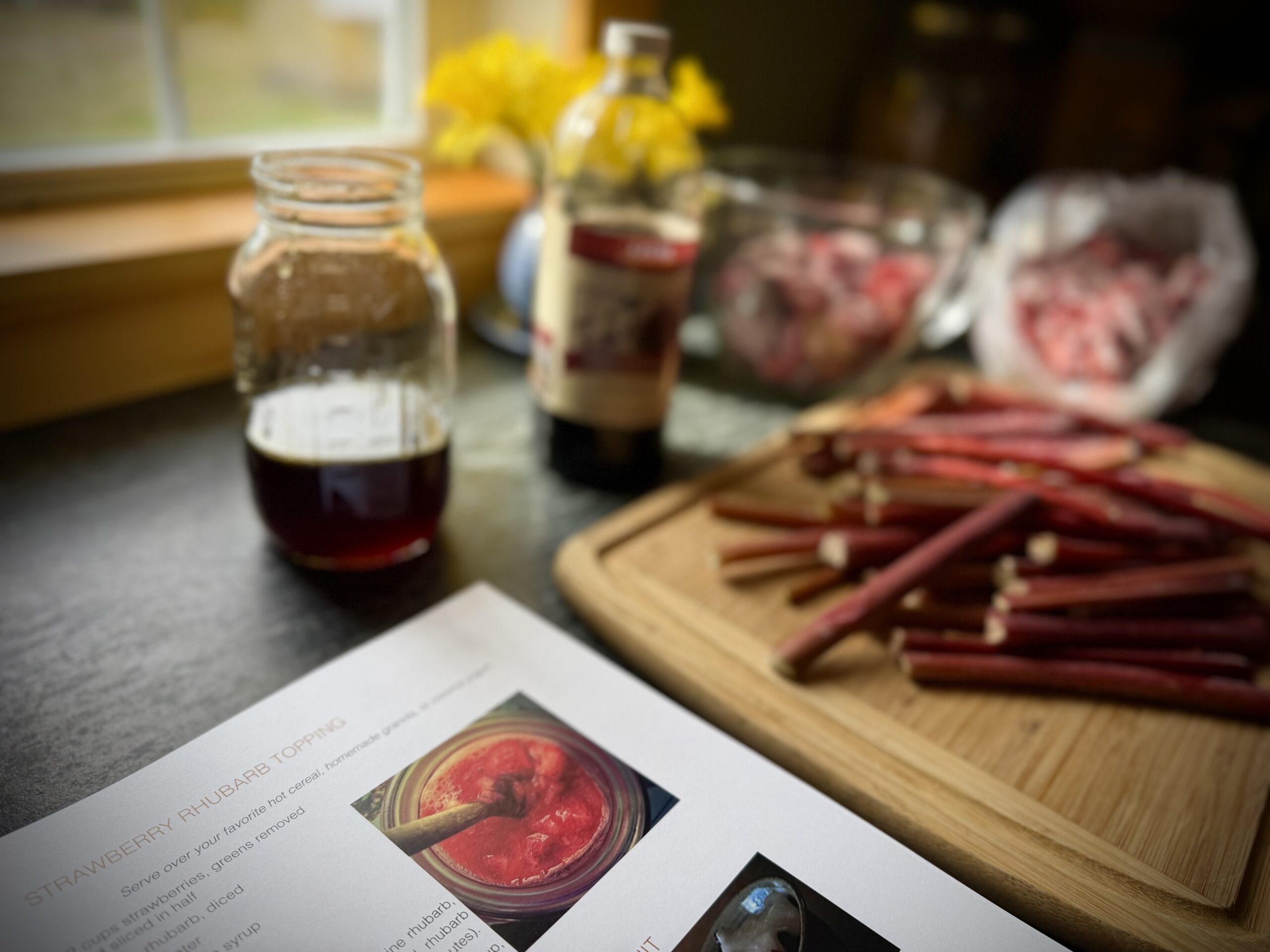 Rhubarb stalks on a cutting board with strawberries and maple syrup in a home kitchen, preparing strawberry rhubarb topping