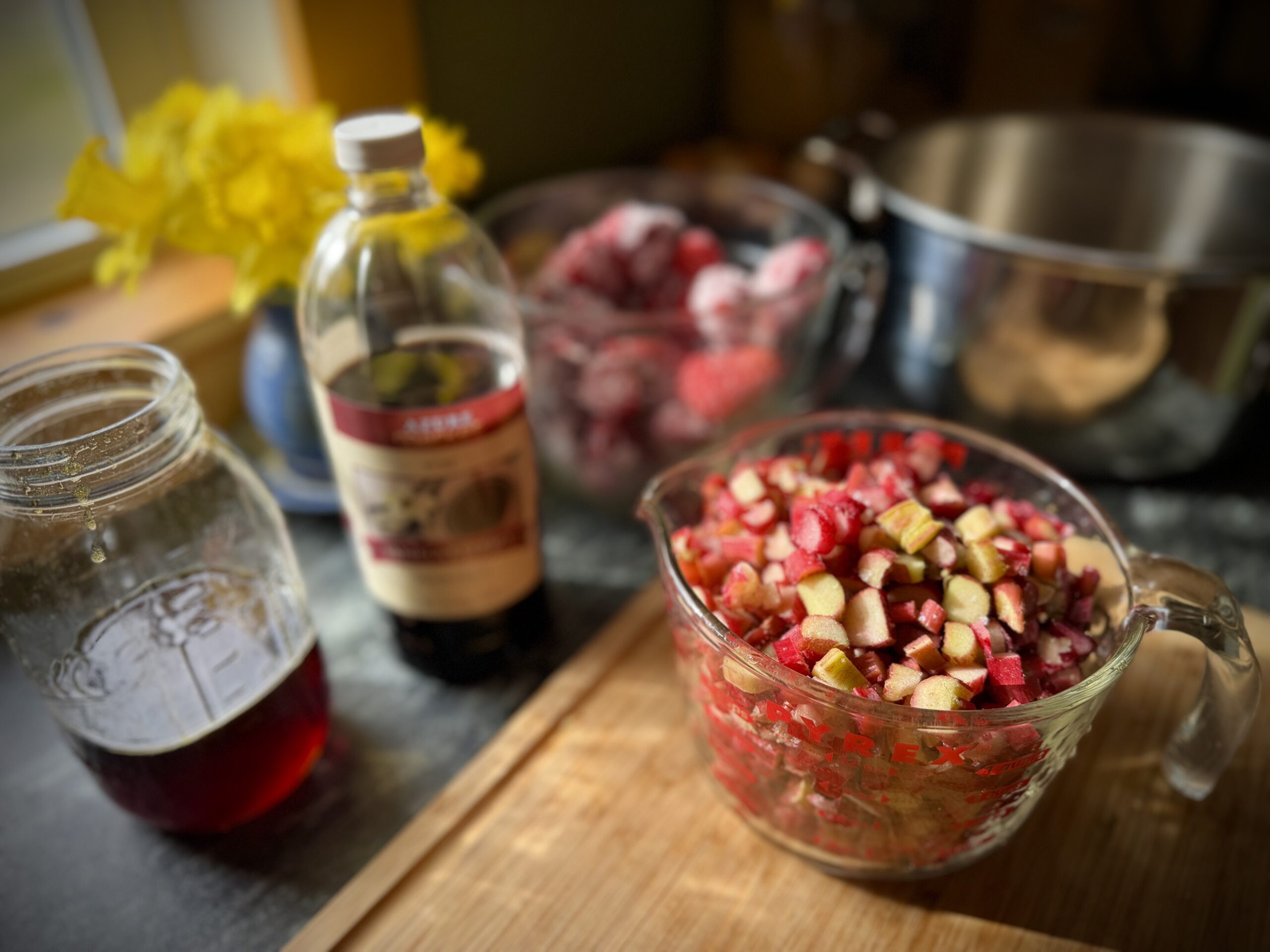 Chopped strawberries and rhubarb in a measuring cup with maple syrup and vanilla in a farmhouse kitchen