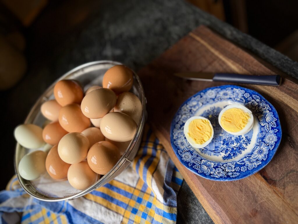 Farm fresh steamed hard boiled eggs in a metal colander with peeled egg halves on a blue transferware plate