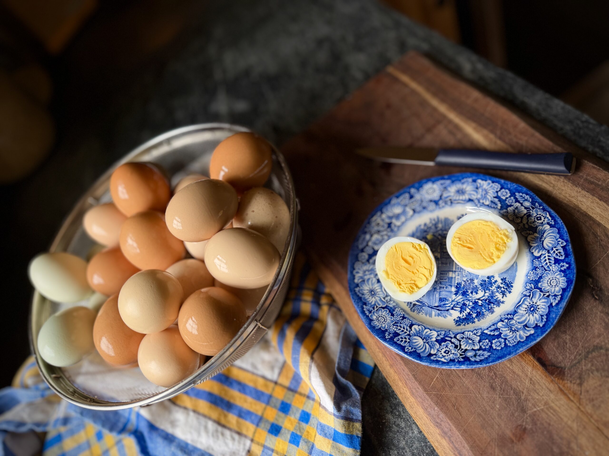 Farm fresh steamed hard boiled eggs in a metal colander with peeled egg halves on a blue transferware plate
