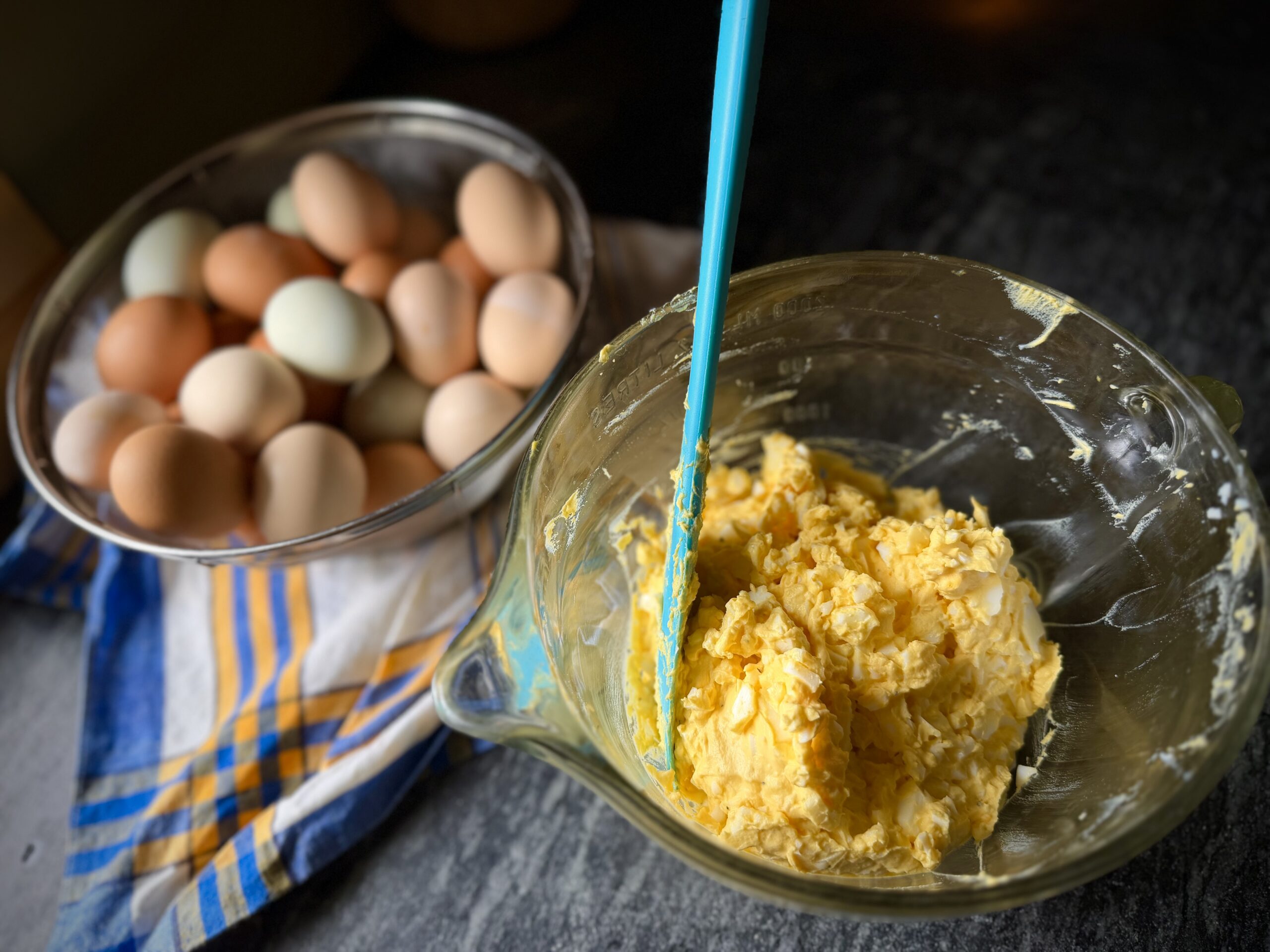 Homemade egg salad being mixed in a glass bowl with farm fresh eggs in a cozy homestead kitchen