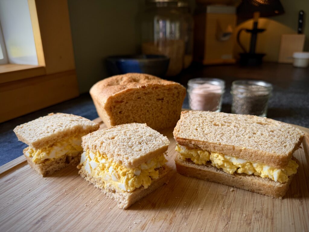 Homemade egg salad sandwiches made with farm fresh eggs and mayonnaise on fresh bread in a cozy homestead kitchen.