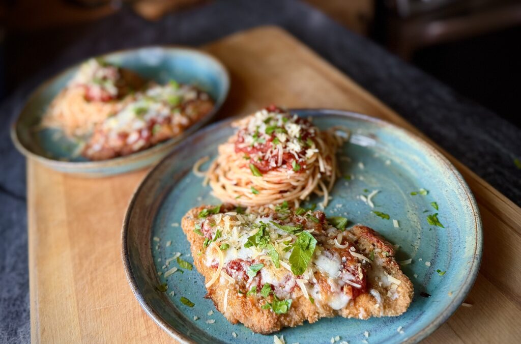 Chicken parmesan served with spaghetti and marinara sauce on a blue plate, topped with melted mozzarella, parmesan cheese, and fresh basil.
