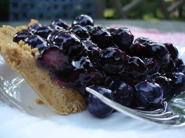 Slice of blueberry glacé pie with fresh blueberries in a graham cracker crust.