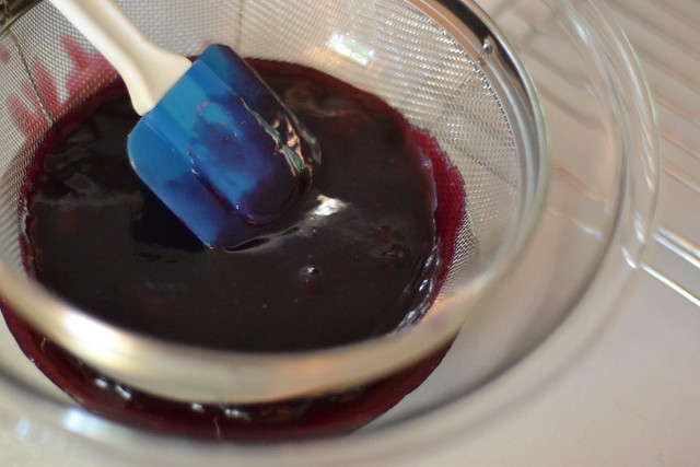 Straining homemade blueberry glaze through a fine mesh sieve for blueberry glacé pie.