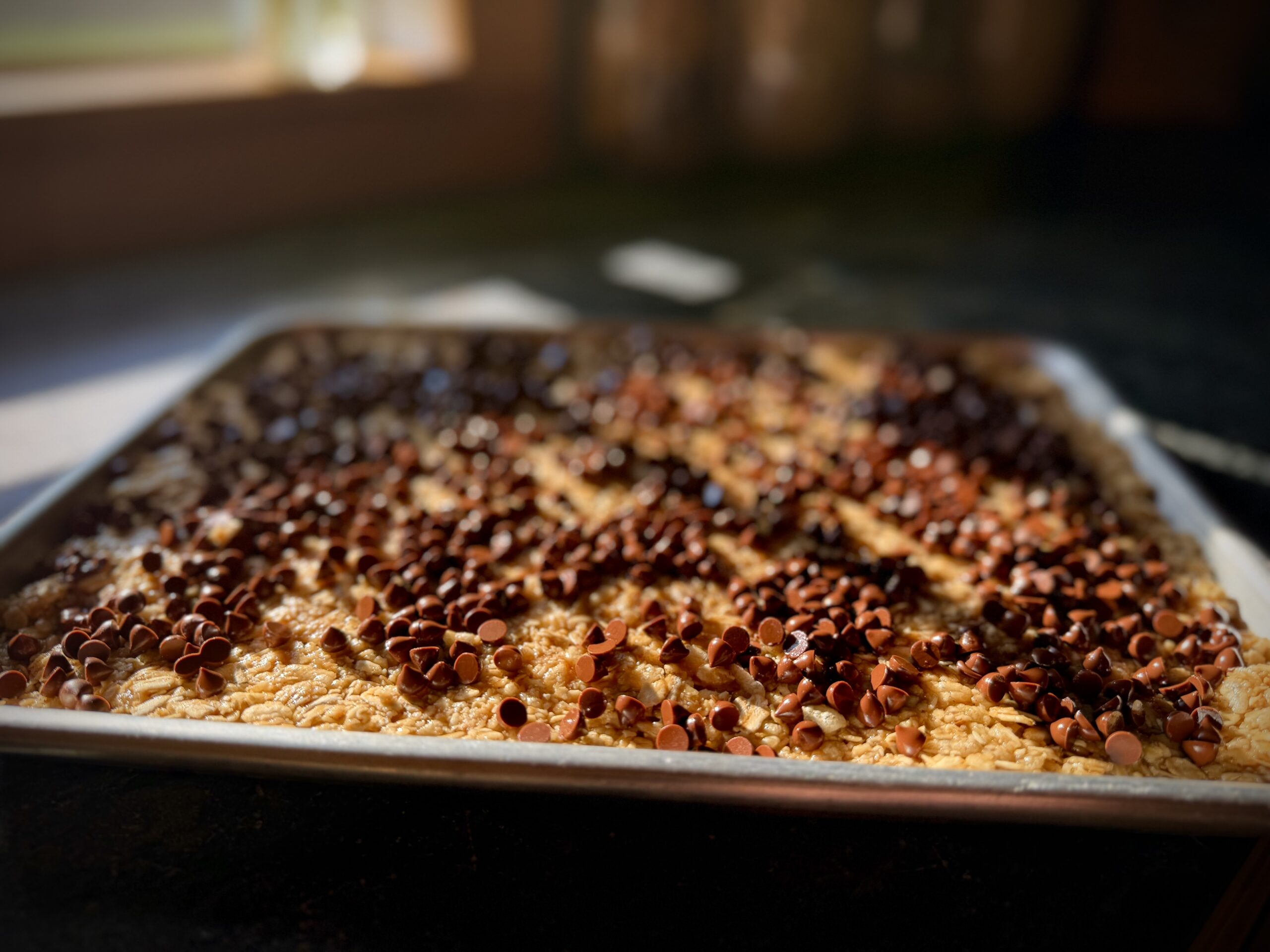 Chewy chocolate chip granola bars pressed into a baking pan and topped with mini chocolate chips before chilling.