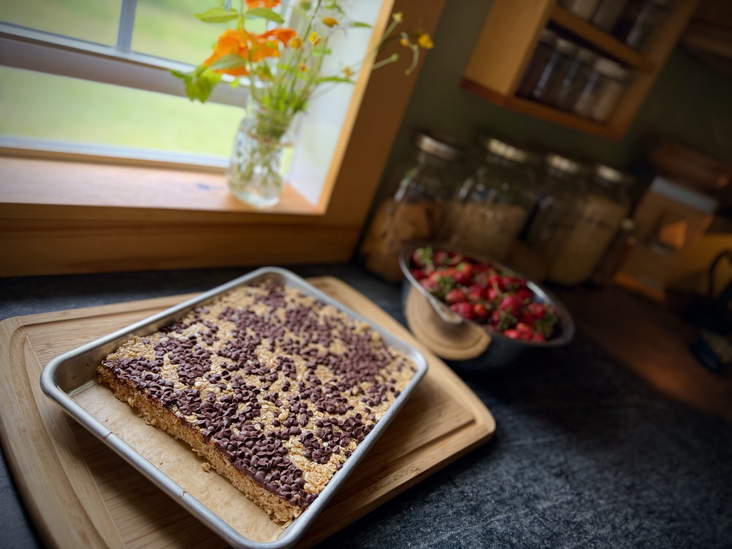 Pan of chewy chocolate chip granola bars cooling by a sunny kitchen window before cutting into bars.