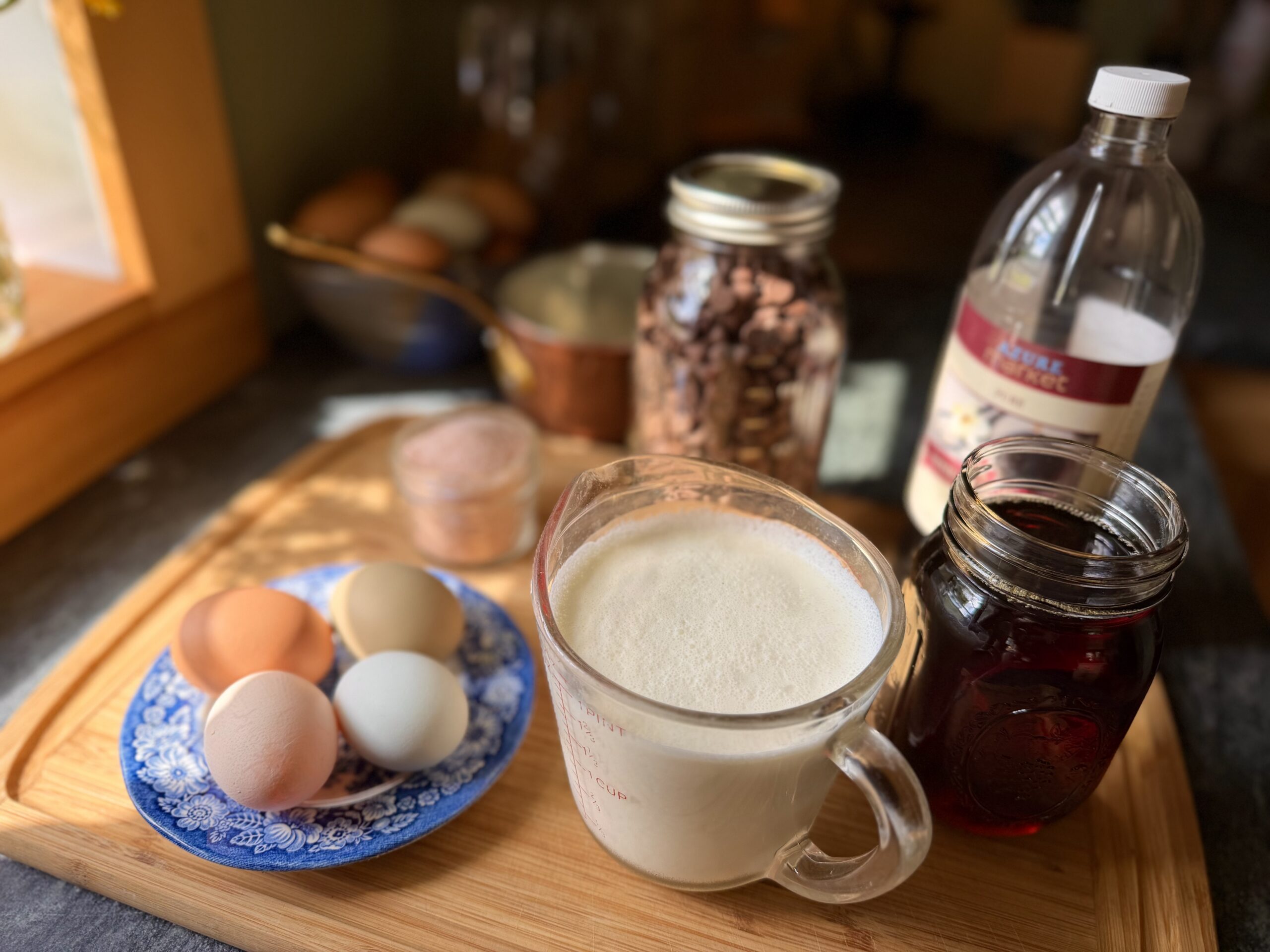Simple ingredients for homemade chocolate mousse, including eggs, heavy cream, maple syrup, chocolate chips, vanilla, and sea salt.