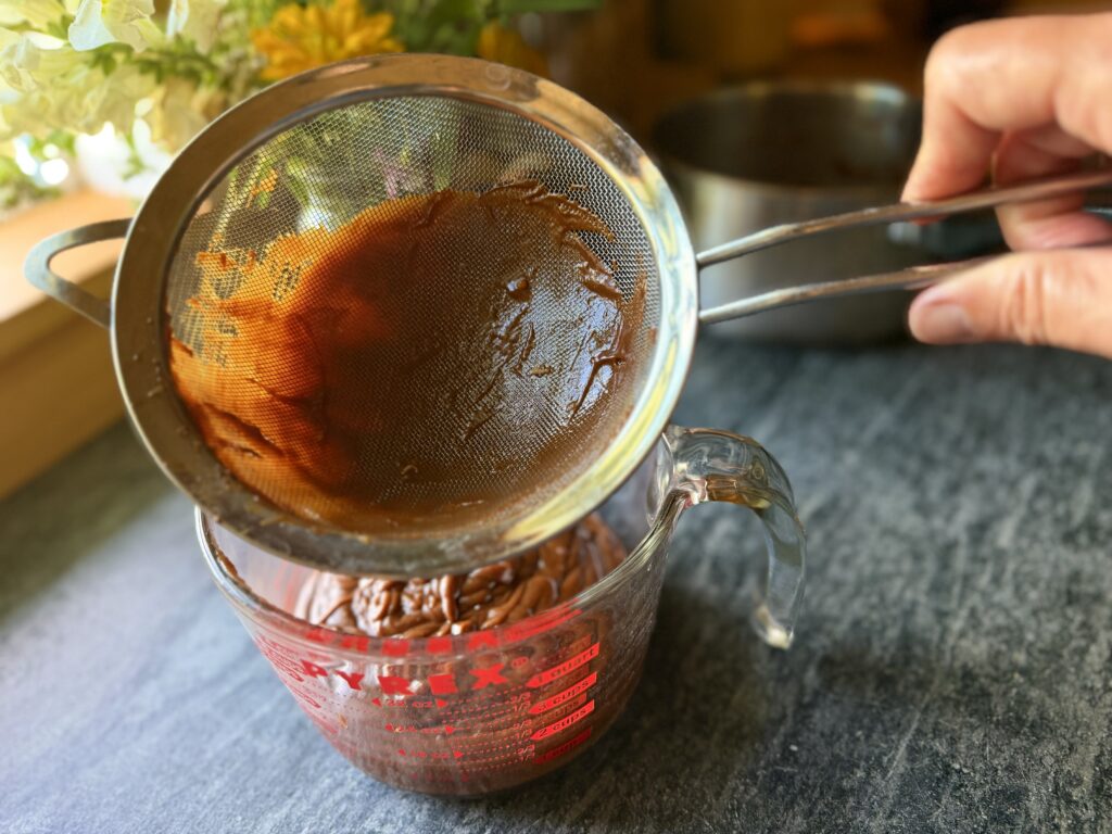 Straining chocolate custard through a fine mesh sieve for homemade chocolate mousse.