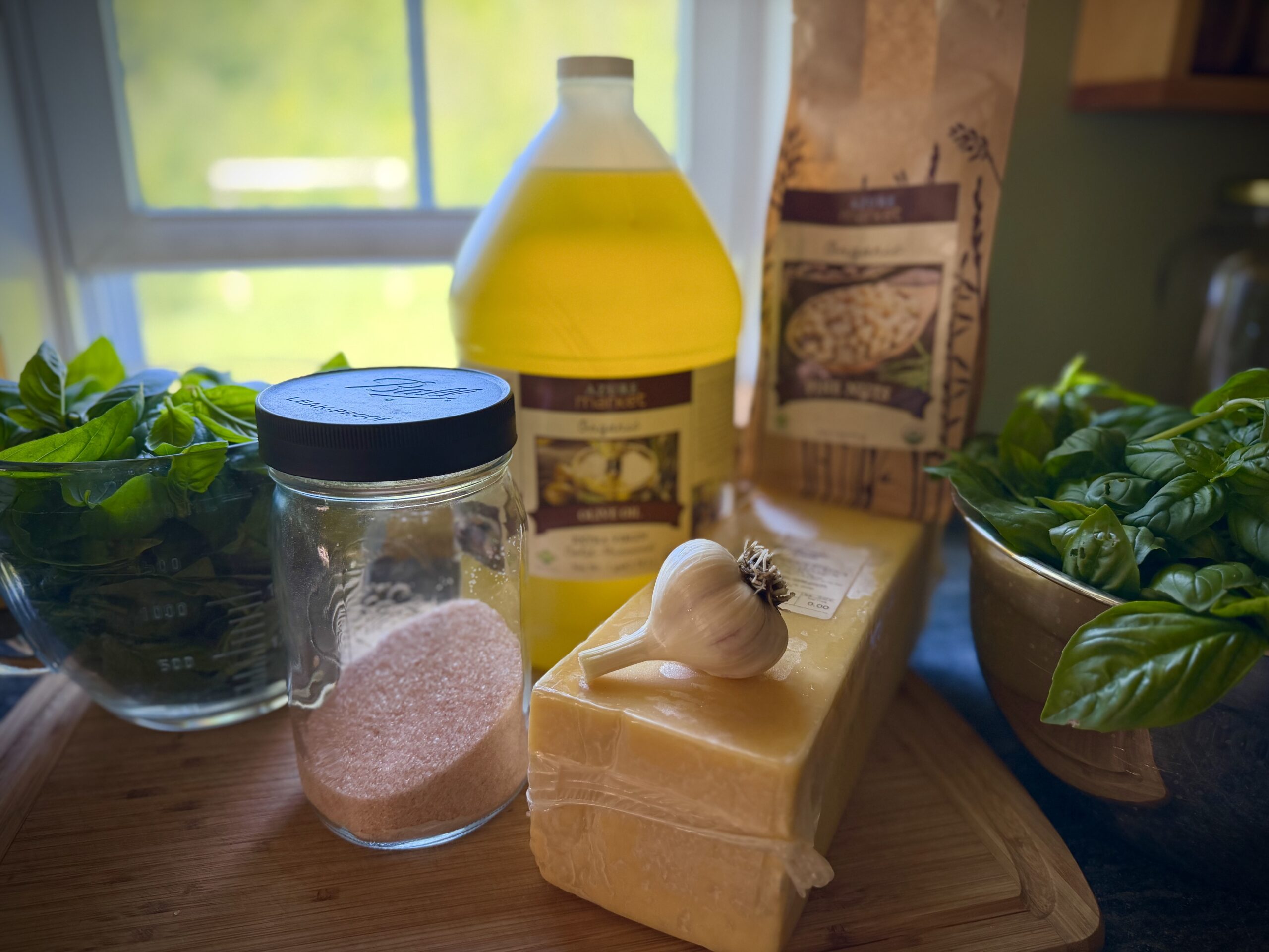 Fresh basil, Parmesan cheese, garlic, olive oil, and sea salt arranged on a wooden cutting board for making homemade basil pesto.