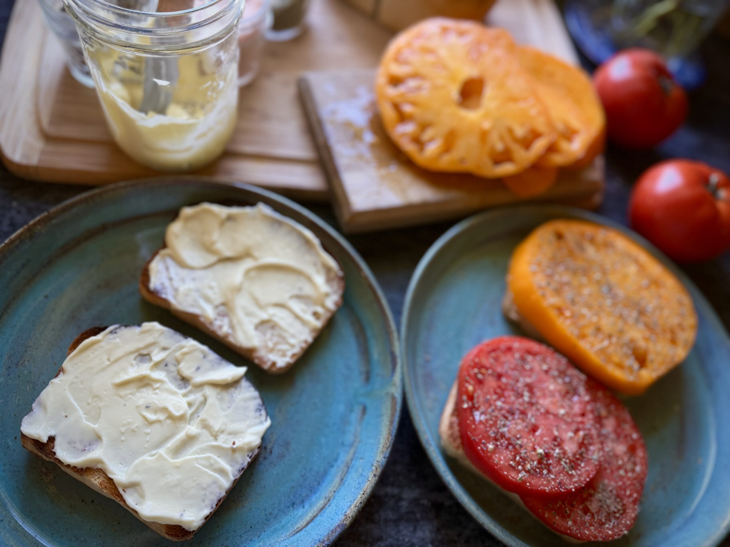 Toasted bread spread with mayonnaise beside seasoned fresh tomato toast