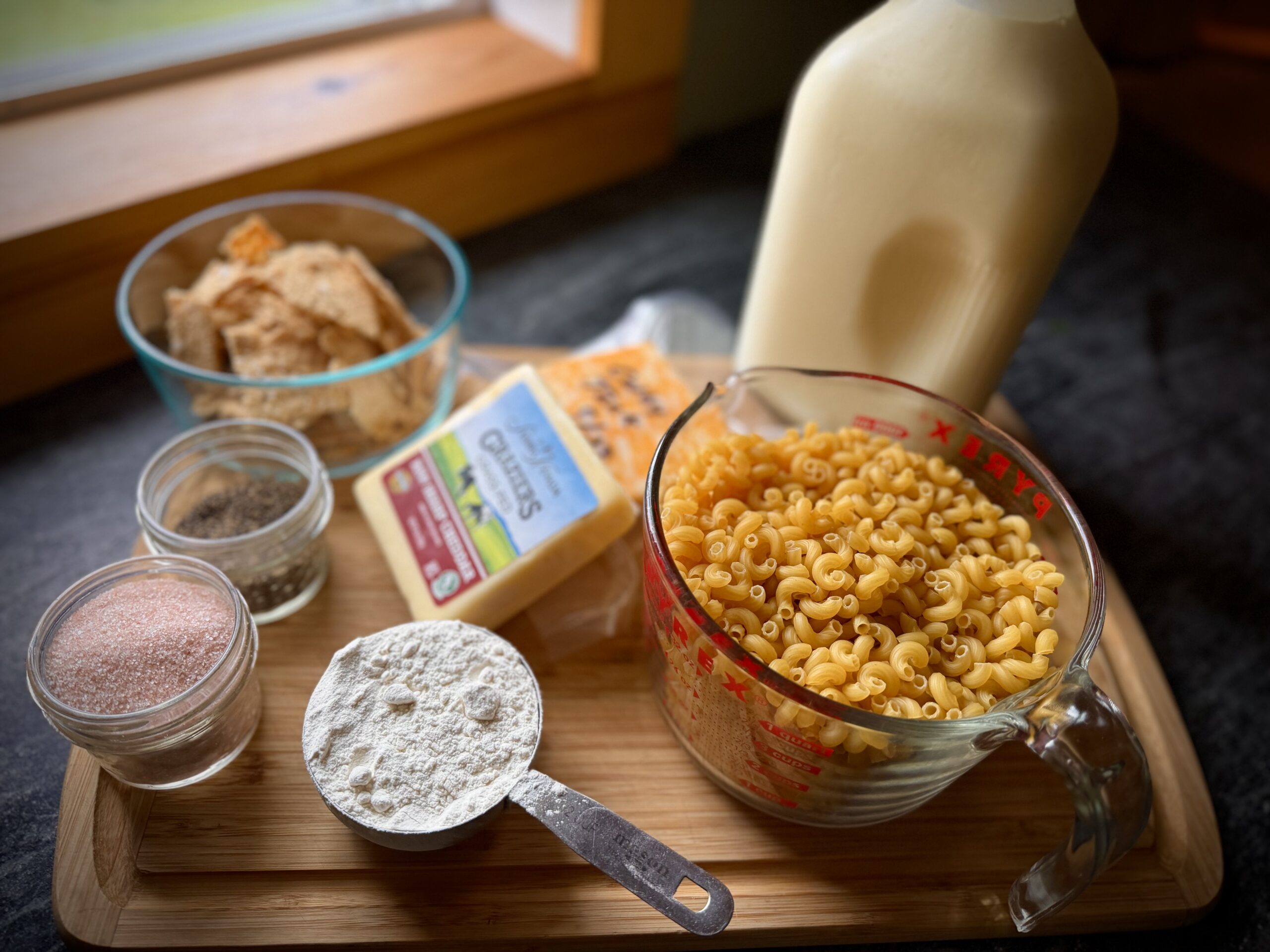 Ingredients for homemade macaroni and cheese including pasta, milk, cheddar, flour, seasonings, and crackers