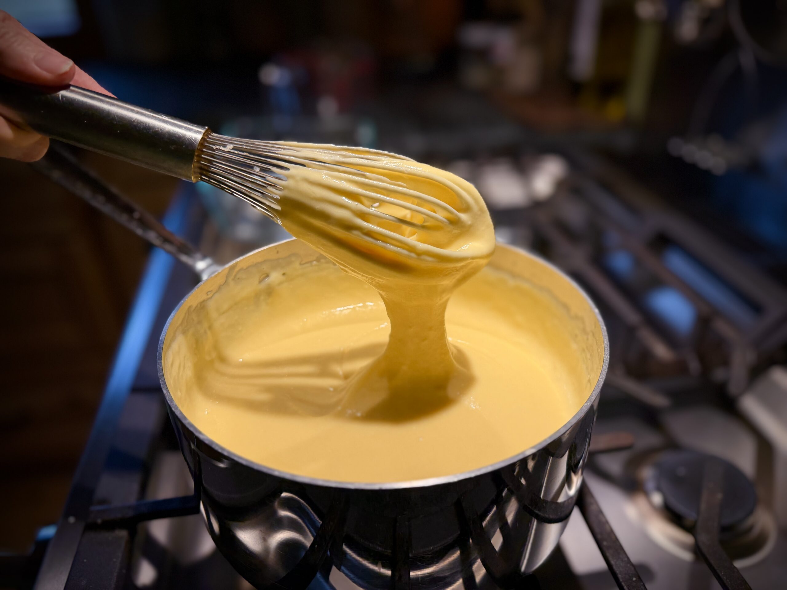 Finished cheese sauce for classic farmhouse macaroni and cheese coating a whisk