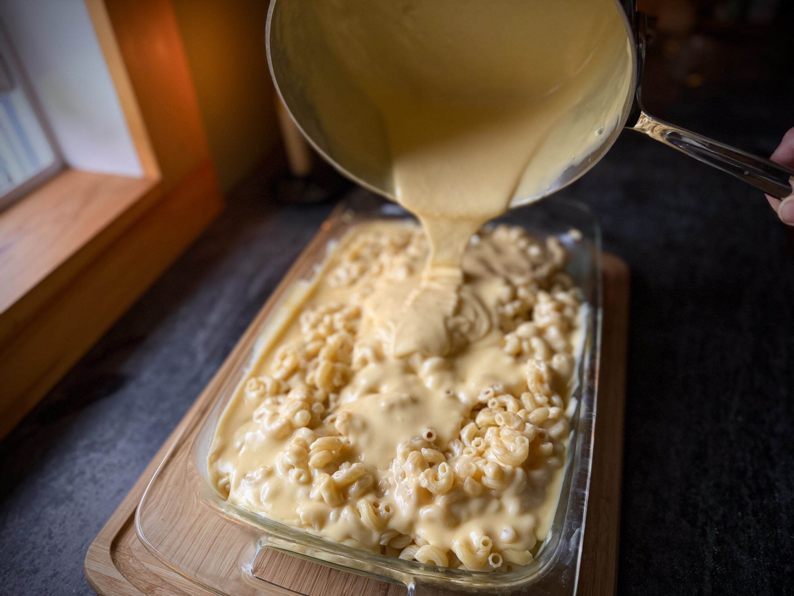 Homemade cheese sauce being poured over macaroni for classic farmhouse macaroni and cheese