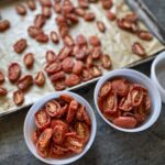 Oven-roasted Juliet tomatoes on a parchment-lined baking sheet, with two small containers filled for freezer storage.