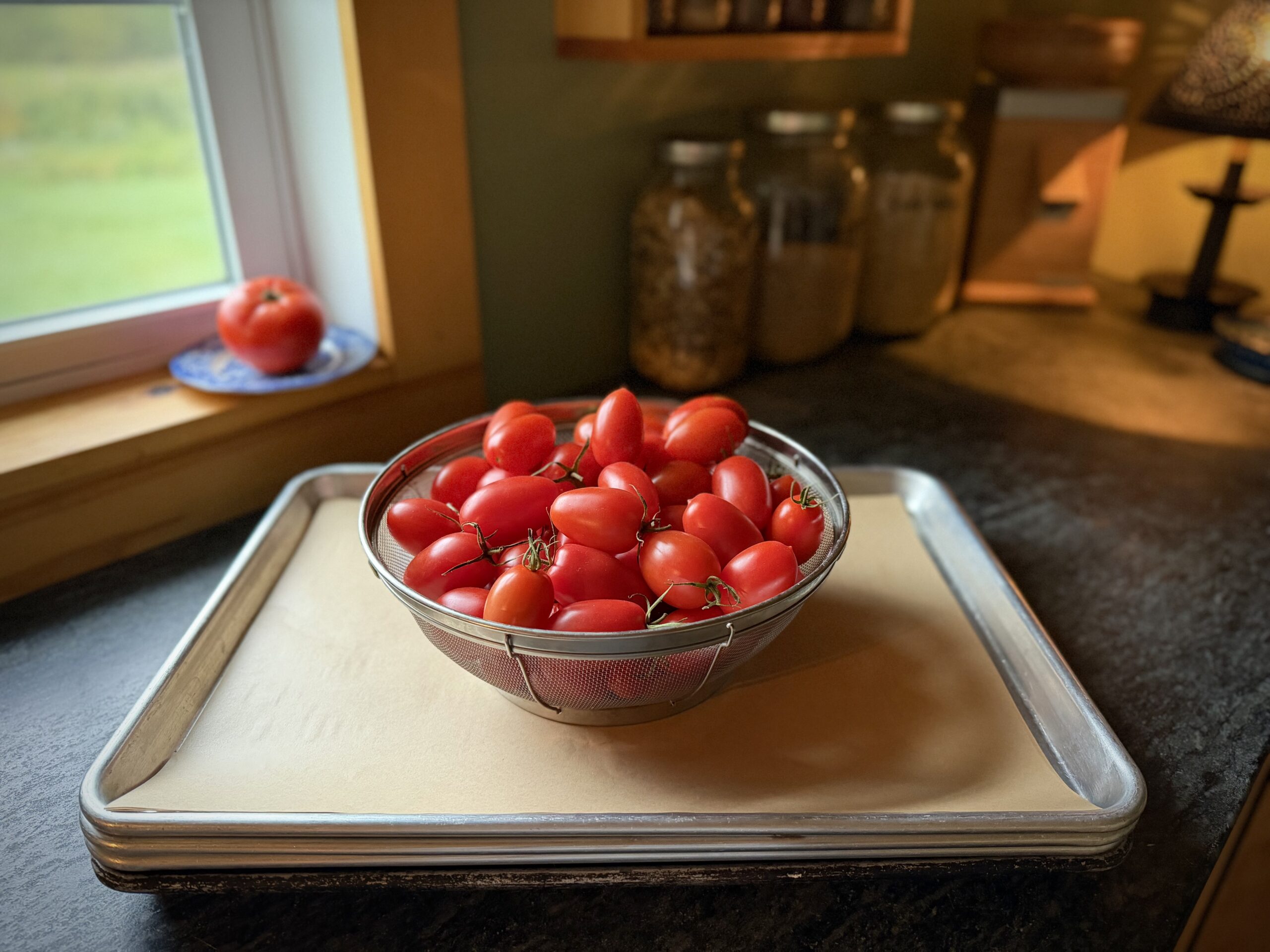 Freshly harvested Juliet tomatoes in a metal colander, resting on a parchment-lined baking sheet in a farmhouse kitchen.