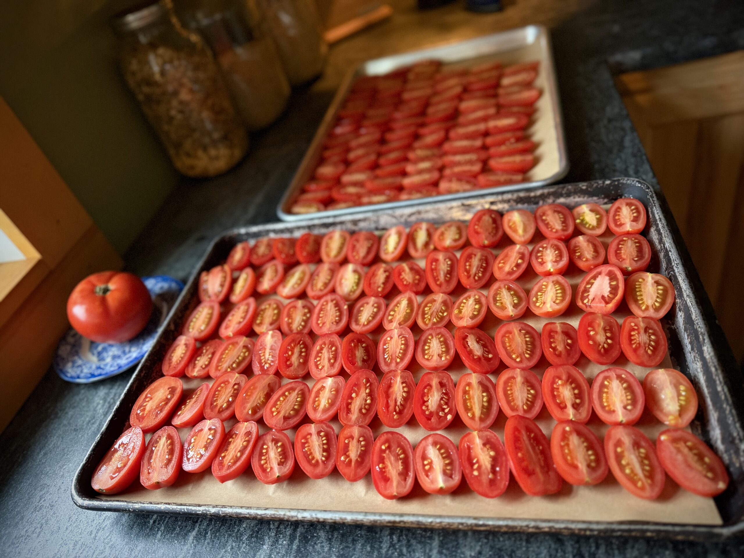 Fresh Juliet tomatoes sliced lengthwise and arranged cut-side up on two parchment-lined baking sheets, ready for oven roasting.