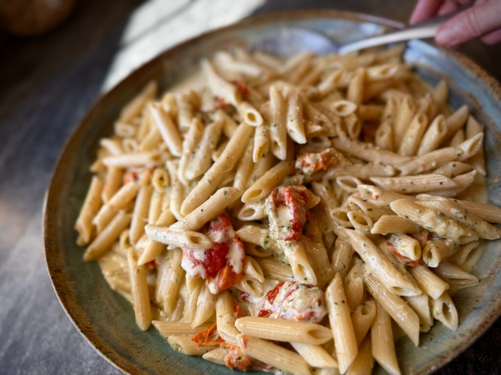 Penne pasta tossed with basil pesto, Parmesan, and oven-roasted tomatoes in a rich sauce, served on a large rustic blue platter.