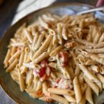 Penne pasta tossed with basil pesto, Parmesan, and oven-roasted tomatoes in a rich sauce, served on a large rustic blue platter.