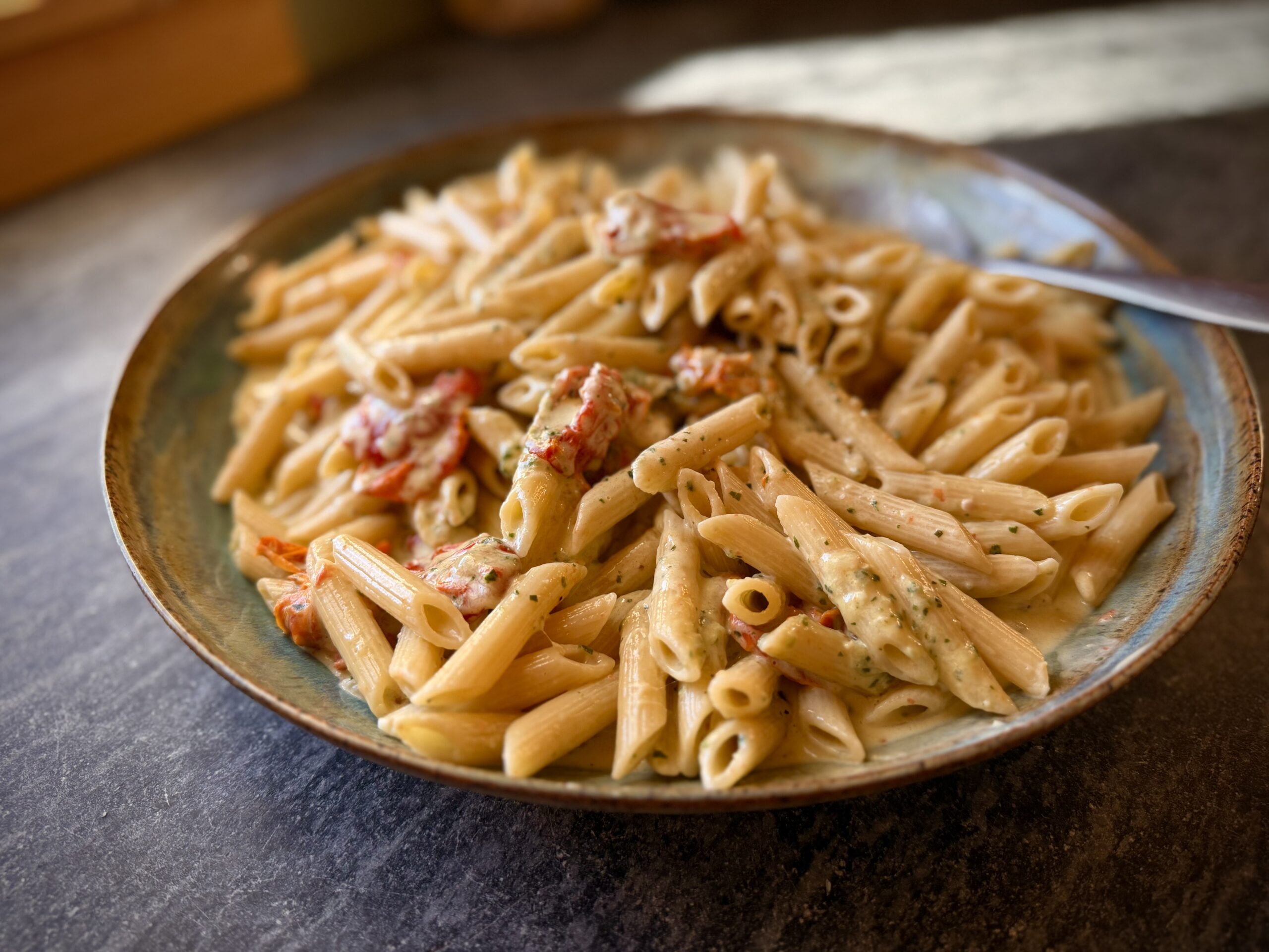 Homemade pesto penne pasta with oven-roasted tomatoes and Parmesan cheese, served in a shallow blue ceramic bowl.