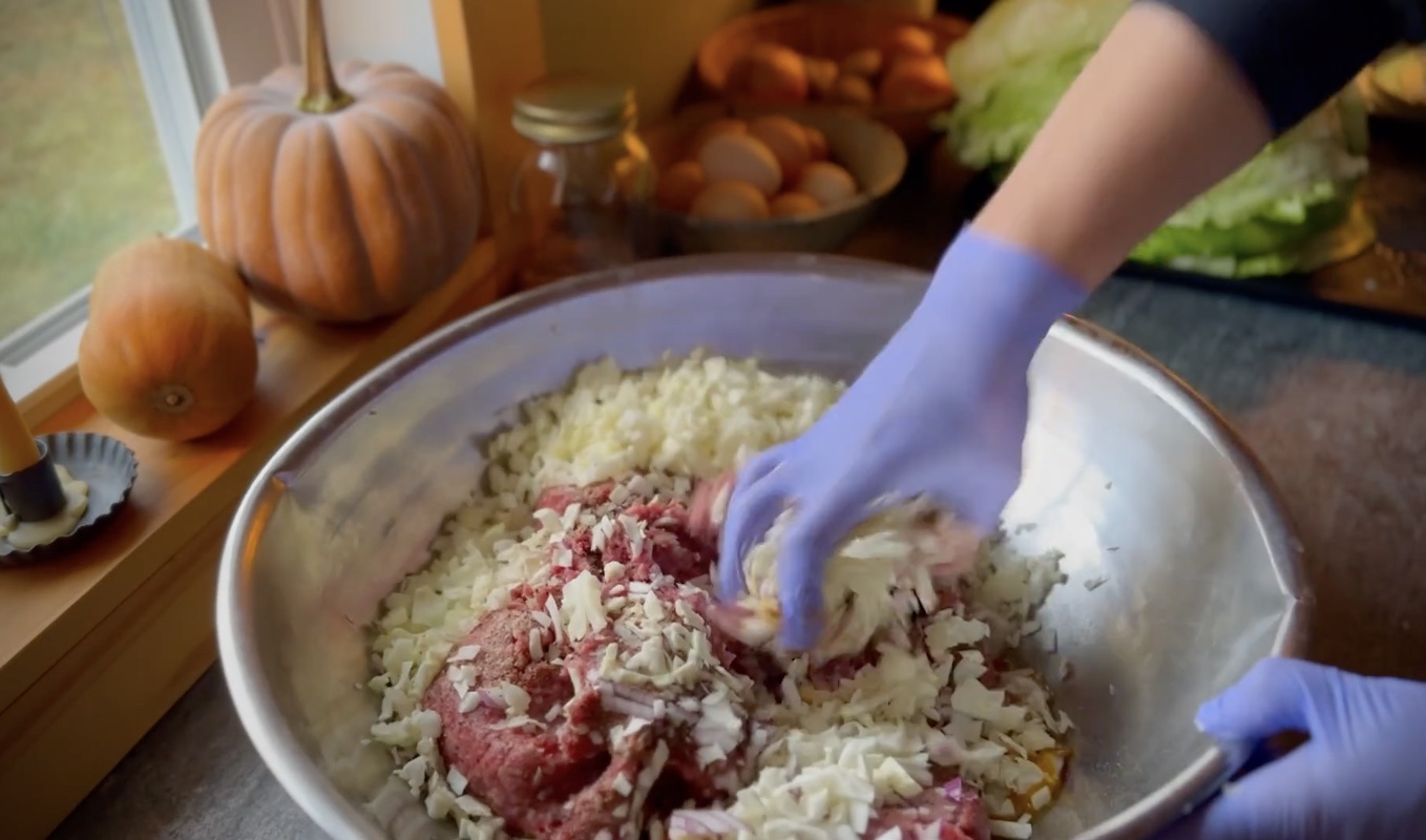 Ground beef filling for stuffed cabbage rolls being mixed by hand with chopped onion, cabbage and eggs.